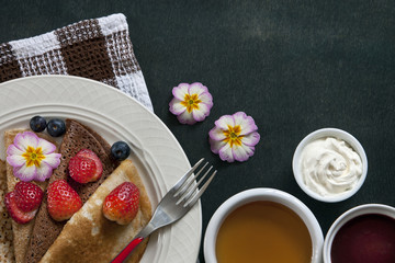 Close-up of homemade pancakes with strawberries on white plate with cup of tea on table with vintage fork. Top view