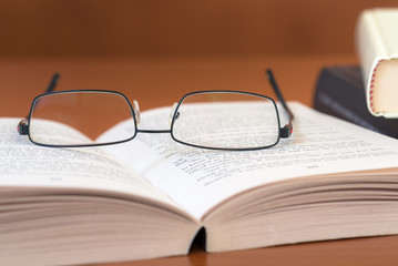 Pair of Glasses on a Textbook Lying Open on a Wooden Desk. Concept of Learning and Education.