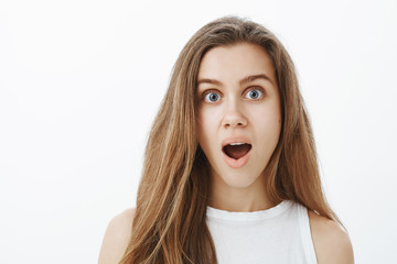 Close-up portrait of impressed surprised attractive woman with fair hair, dropping jaw and staring shocked at camera, seing something unvelievable and cool, standing over gray background