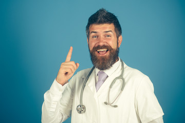 Medical and healthcare concept - friendly bearded doctor with stethoscope in white coat raised finger up. Cheerful physician with stethoscope on neck. Smiling handsome male doctor in medical gown.