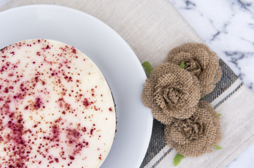 Close up of a red velvet cake, decorated with hessian flowers on a marble background 