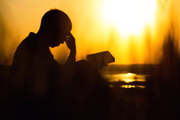 silhouette of a young man with a Bible, male praying to God in nature, the concept of religion and...