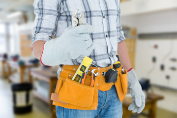 Technician with tool belt around waist holding pliers against workshop