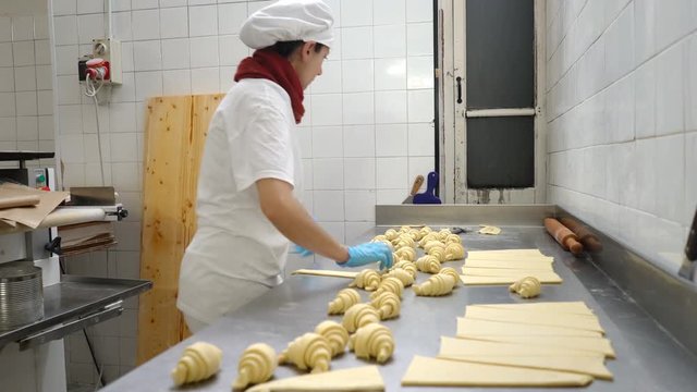 Traditional Italian family bakery. A female baker turns beautiful croissants before baking. Real people.