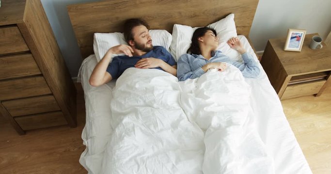 Top view on the young Caucasian attractive man abd woman waking up in the morning and stretching in the bed while lying. Indoors