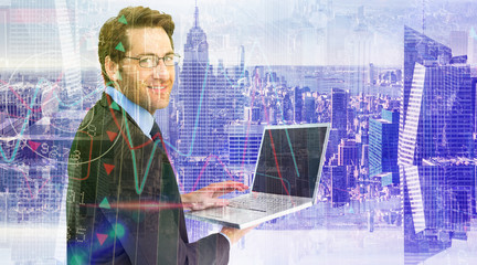 Smiling businessman using a laptop  against room with large window looking on city