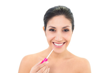 Brunette applying lip gloss and smiling at camera