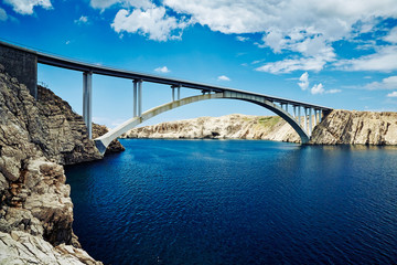 A concrete bridge connecting two Croatian islands against a blue sky. White clouds in the sky and blue sea.