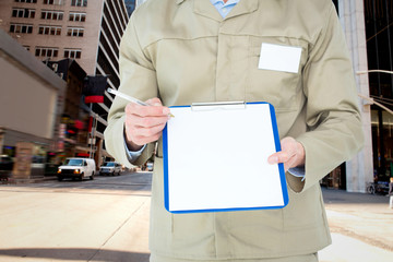 Delivery man showing blank paper on clipboard against new york street