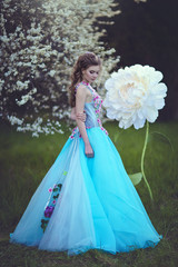 Fototapeta premium A beautiful girl like Thumbelina in a blue fluffy dress near a giant peony flower. Blonde with huge fairy flowers.