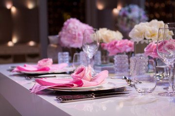 Beautiful table setting with a white tablecloth and pink napkins. Red cutlery, beautiful dining utensils. Wedding Decor Textiles