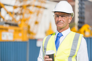 Engineer builder on construction site at sunny day with coffee in hand