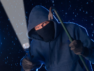 Dangerous burglar using a crowbar to break into a house late at night, home safety concept
