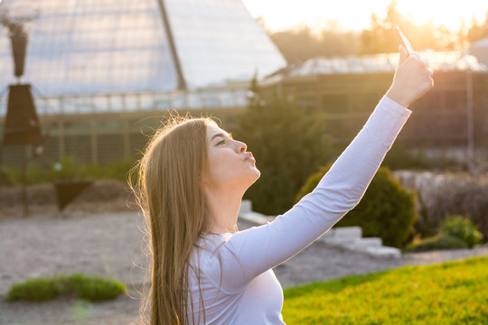 Young beautiful female student taking a duck-face self in the park at sunset
