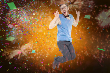 Fototapeta na wymiar Geeky hipster jumping and smiling against colourful fireworks exploding on black background
