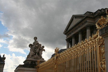 The golden fence with royal crown, statue and Versailles palace in the cloudy sunny day