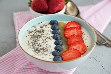 Fresh and healthy breakfast - oats porridge bowl with fresh berries and chia seed. On grey table. Natural light, selective focus.