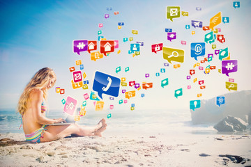 Gorgeous blonde in bikini using laptop on the beach with colourful computer applications