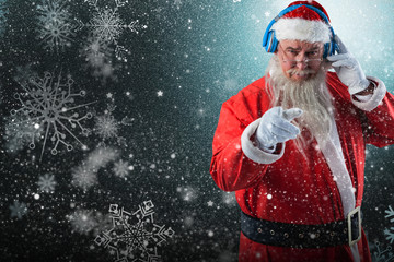 Portrait of Santa Claus listening to music on headphones while pointing against snowflake pattern