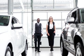 African man with a girl standing between two new cars in the showroom