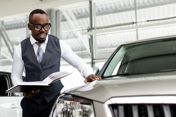 African man with glasses inspects a new car in the showroom