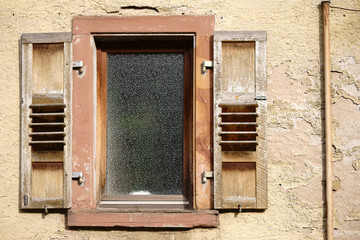 Vergilbte Fassade und Fenster / Ein heruntergekommenes Wohnhaus mit einer vergilbten Fassade sowie abblätternden Farb-und Putzschichten am Fenster sowie an Fensterläden.