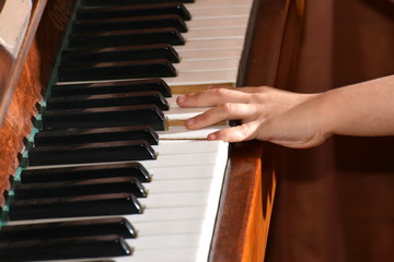 The boy plays the brown piano on notes.