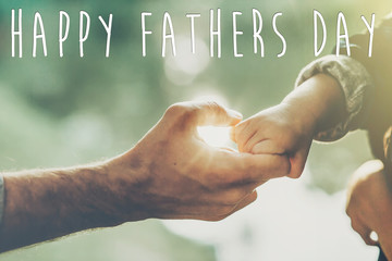 happy father's day text, greeting card concept. father and little son holding hands in sunlight in...