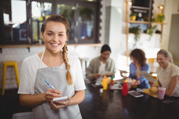 Portrait of smiling young waitress with notepad at cafe