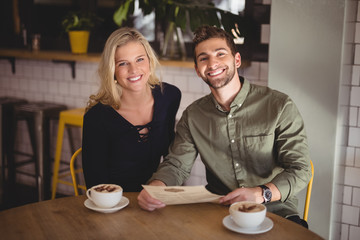 Smiling young couple sitting with coffee cups and menu at table