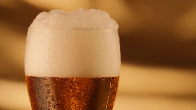 Closeup of rotating fresh beer with abstract golden background and drops on glass