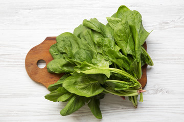 Washed fresh spinach leaves on wooden board on white wooden background. Top view