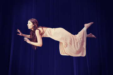 Full length of woman levitating  against red curtain
