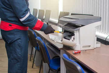 The specialist repairman serves or repairs the laser printer with a screwdriver and a brush....