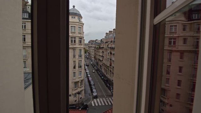 Timelapse shot of people and cars traffic in the street of Paris on overcast and rainy day. View through the house window on upper floor