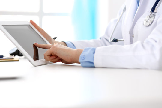 Woman doctor using tablet computer while sitting at the desk in hospital closeup. Cardiologist checks heart diagrams with tablet pc. Healthcare, insurance and smart technology in medicine concept