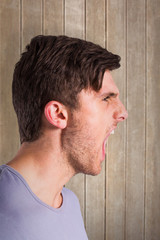 Angry young man with stubble shouting  against wooden surface with planks