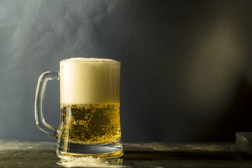 A mug of fresh beer on a dark background of a wooden table.