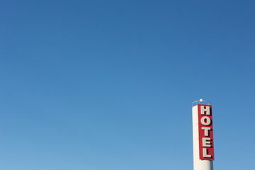 Red and white hotel sign with blue sky background.