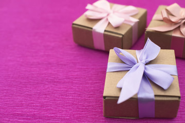 Festive composition three Kraft boxes with gifts on bright pink background.