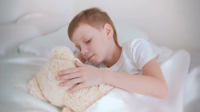 Seven-year-old boy woke up and stroking a toy bear lying in bed.