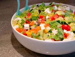 Vitamin-rich salad of sliced leaves and vegetables with cheese flavored with olive oil in a dish with serving spoons