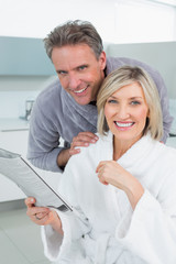Obraz premium Happy couple in bathrobes with newspaper in kitchen