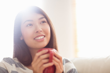 Smiling asian woman on couch having hot drink