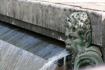 Fountain element with man head and water stream from his mouth in french Versailles