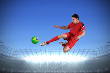Fototapeta na wymiar Fit football player jumping and kicking against large football stadium with spotlights under bright blue