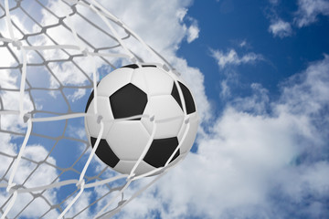 Football at back of net against bright blue sky with clouds