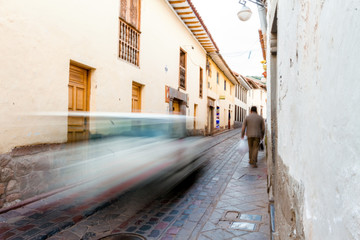 Man walks through the narrow path of an alley in Cusco (Peru) while a car passes quickly