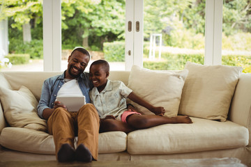 Father and son using digital tablet in living room