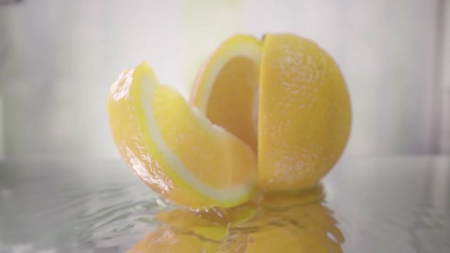 Orange splits into halves on water. Slow motion shot